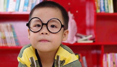 young boy wearing glasses reading in sunday school classroom at church after check-in to children's ministry.